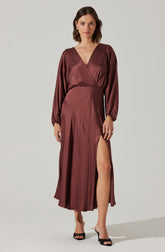 A woman is wearing a long, satin dress in a deep burgundy color. The dress features long, puffed sleeves with elastic cuffs, a V-neckline, and a high slit on the left side that reveals her leg.